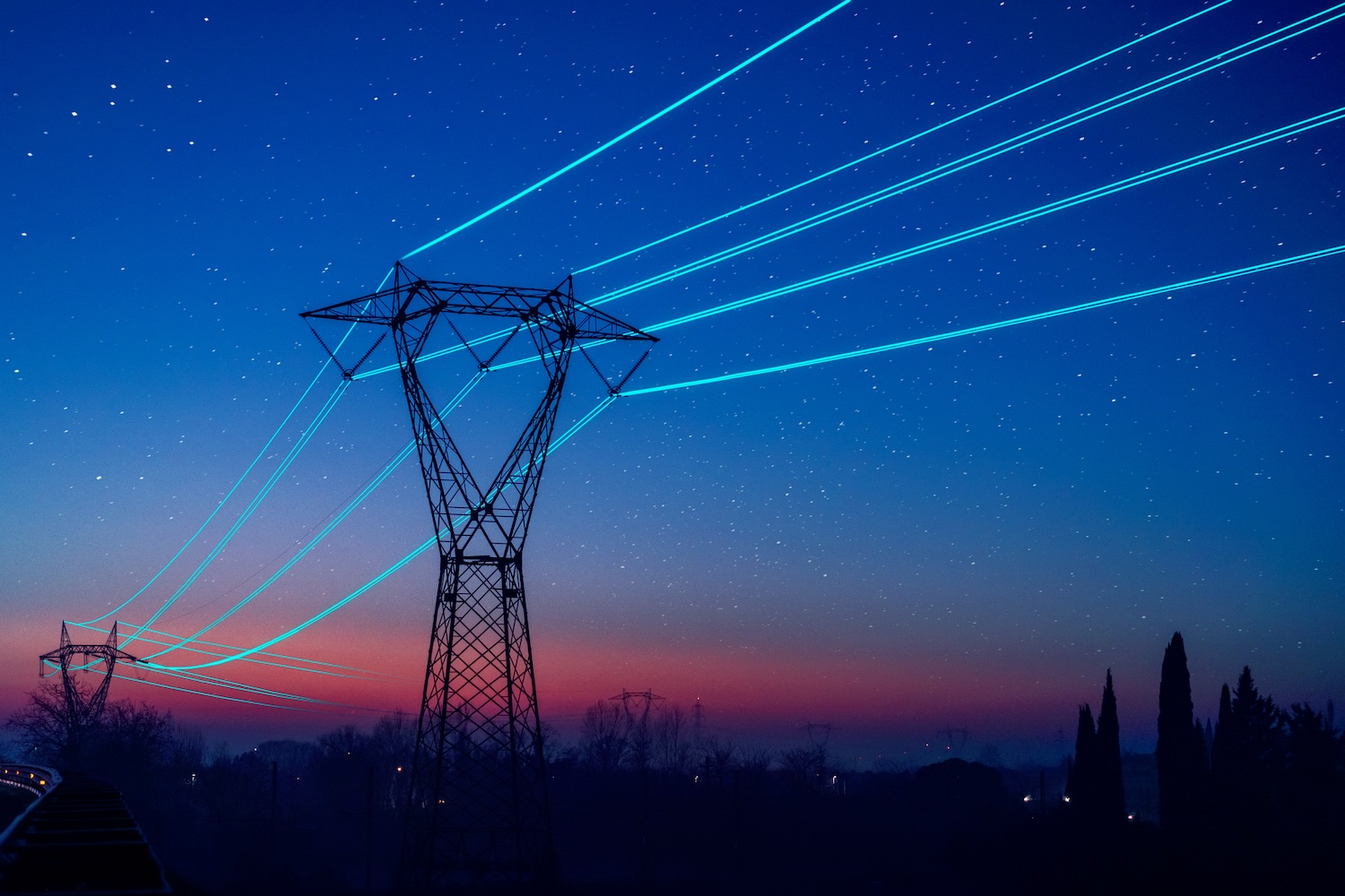 Utility poles with glowing cables over sunset sky