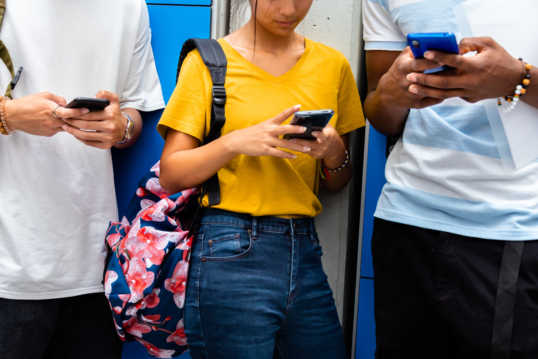 Three people pictured neck down standing against a wall using their mobile phones